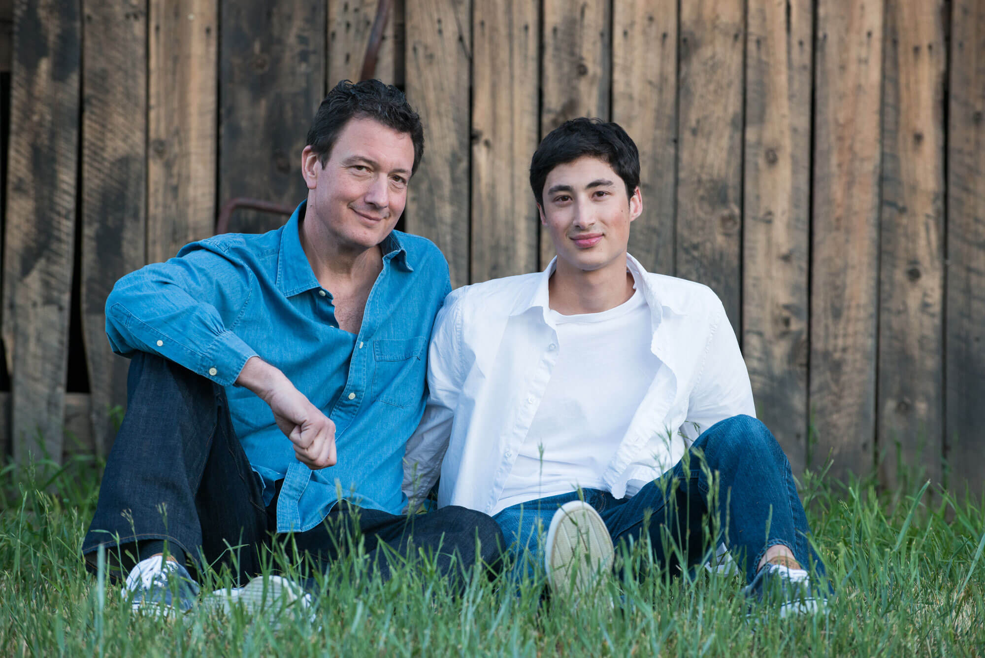 portrait of a father and son sitting in the grass in front of a fence