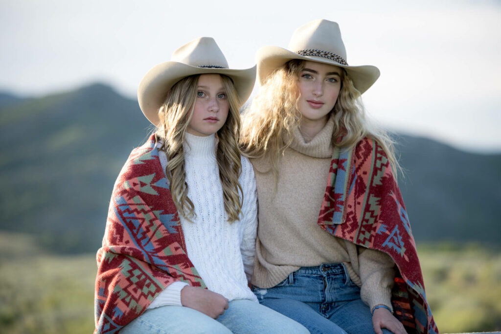 Sisters sitting on a ranch fence